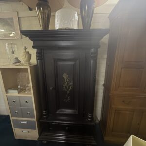 Donkere hoge kast met sierlijsten en bloemdecoratie